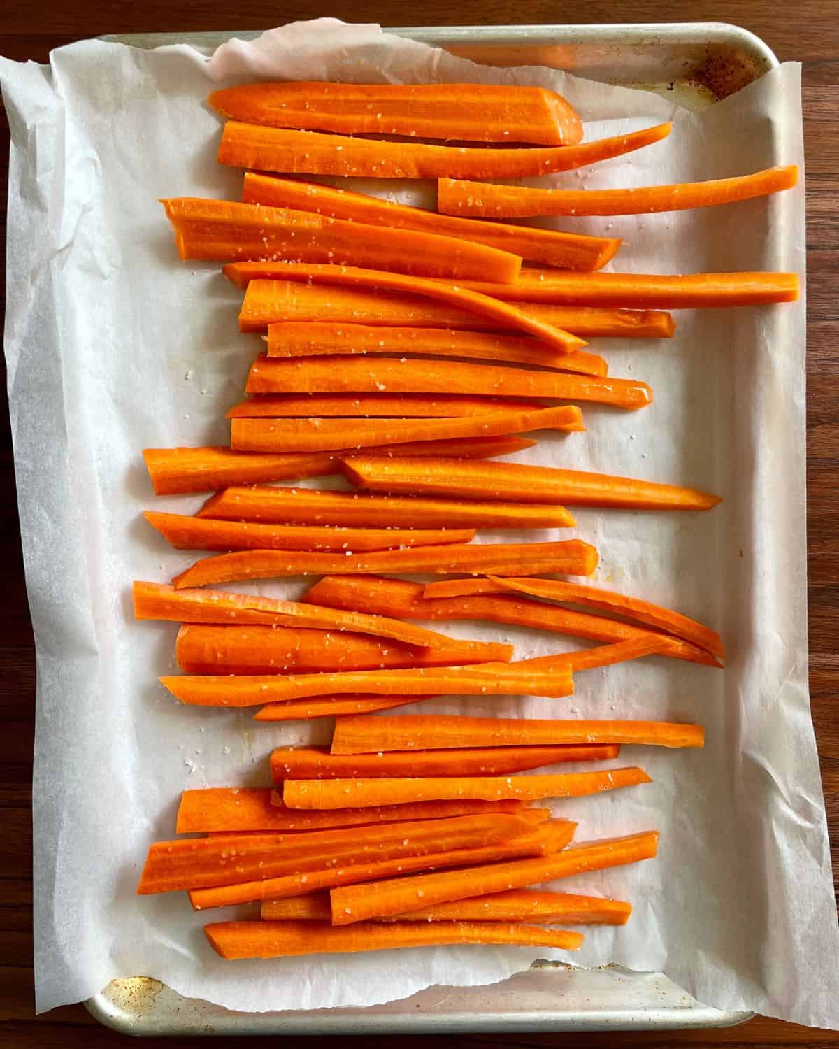 Carrots sliced and laid out on a parchment lined baking sheets drizzled with olive oil and sprinkled with salt.