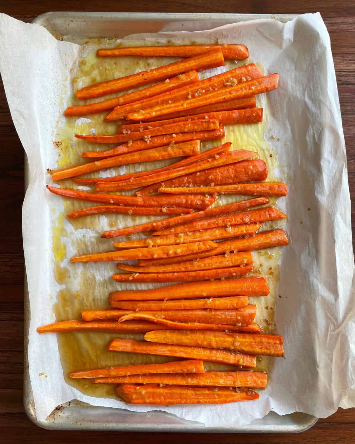 Brown sugar honey glazed carrots cooked on a parchment lined baking sheet.