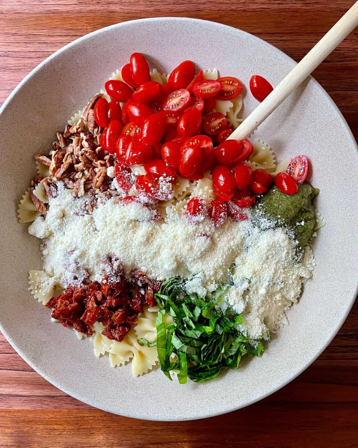 All of the ingredients needed to make pesto pasta sundried tomato salad in a large mixing bowl, ready to be mixed.