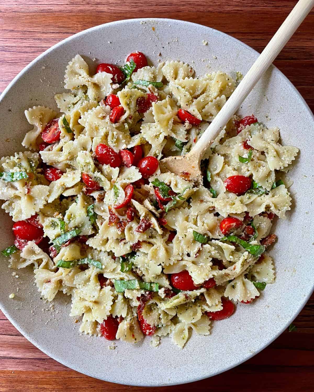 Pesto pasta salad mixed in a bowl with a wooden spoon.