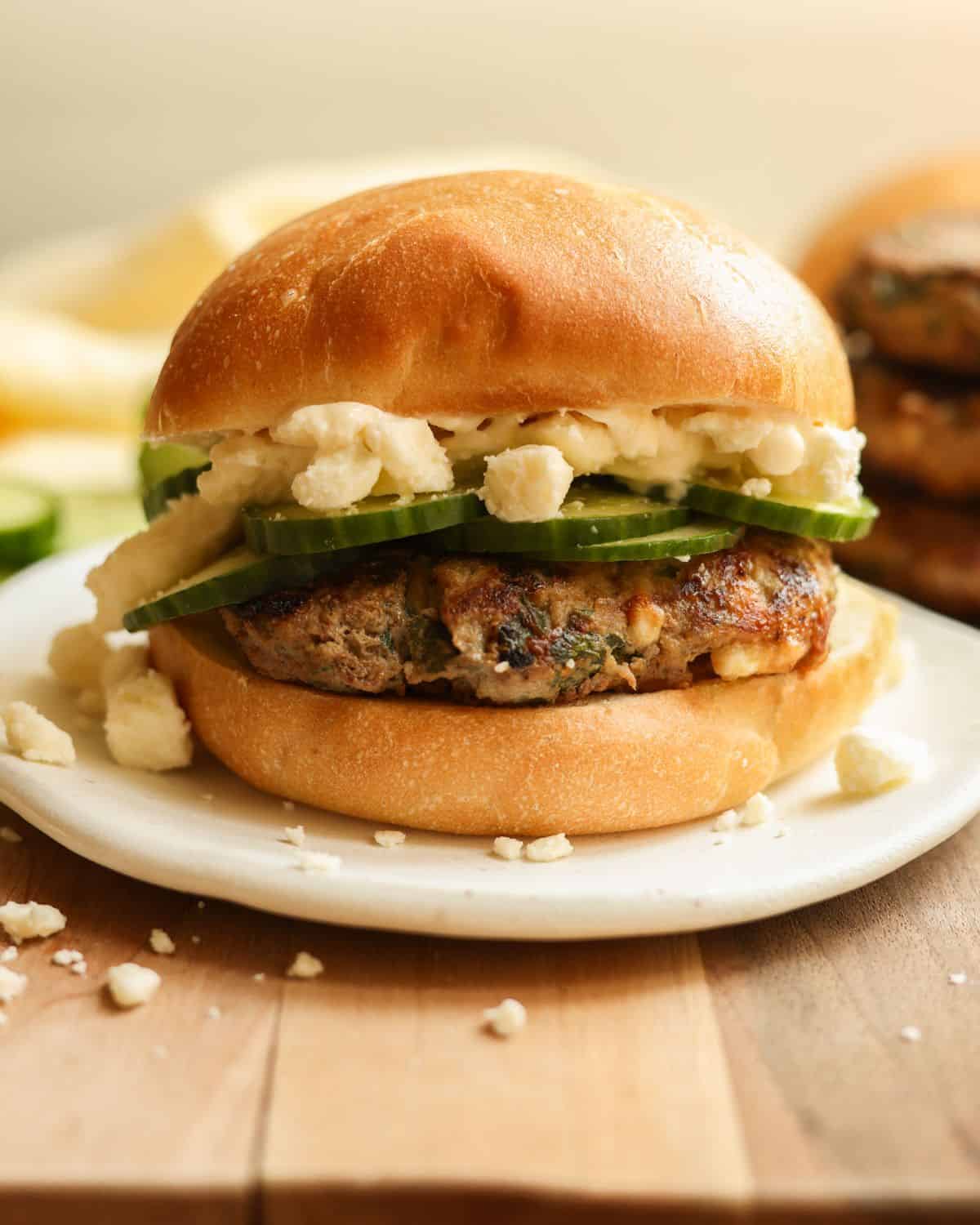 Spinach turkey burger on a bun topped with feta cheese, mayo, and cucumbers.