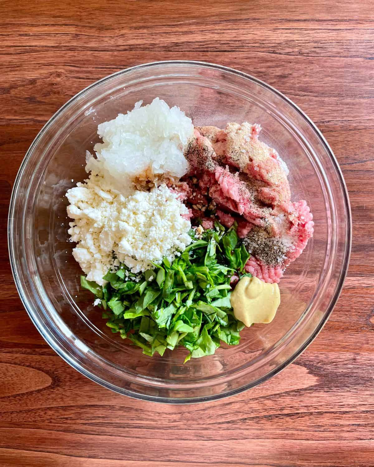 All of the ingredients needed to make turkey burgers with feta and spinach, mixed together in a glass bowl.