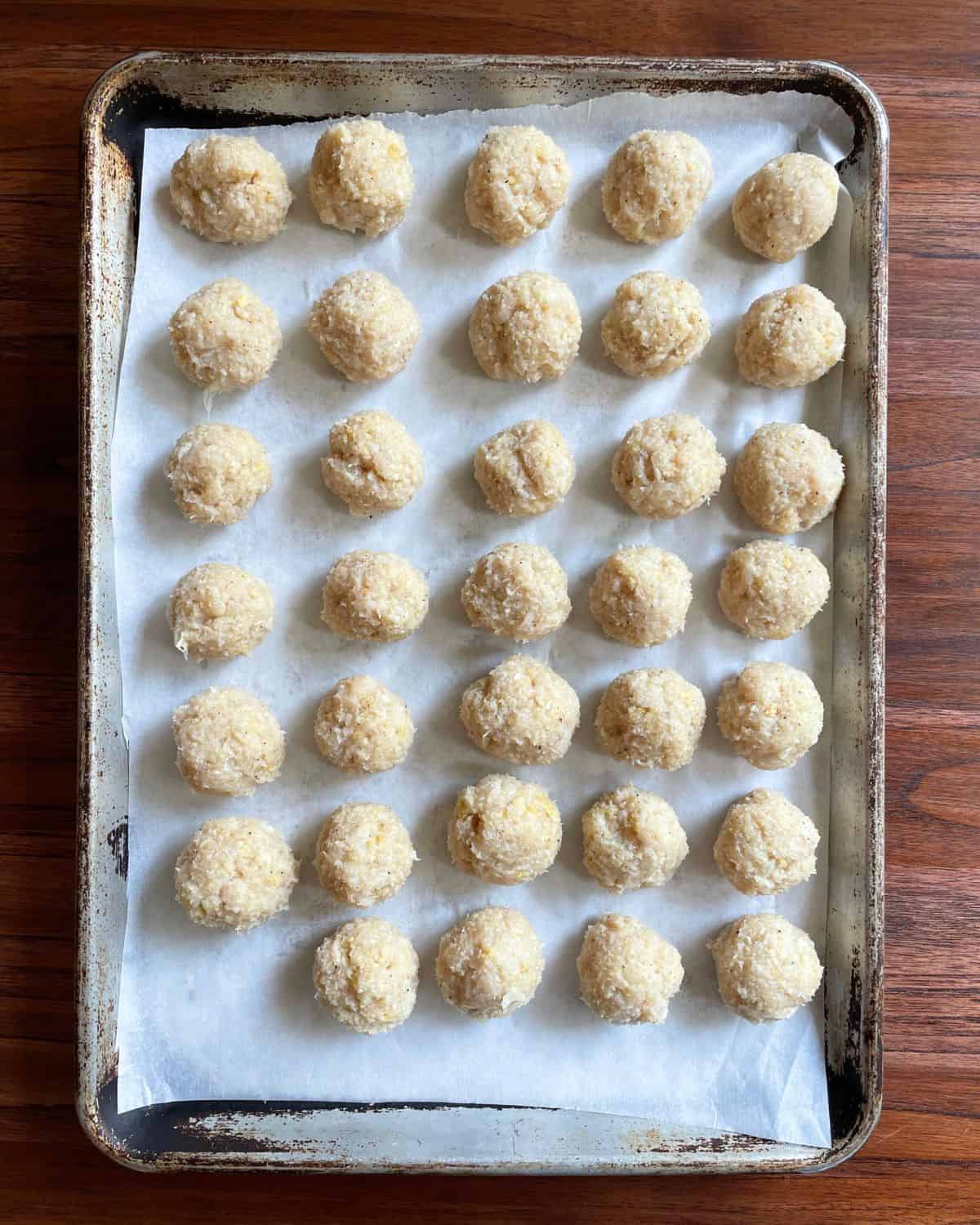 Unbaked ground chicken meatballs on a baking sheet.