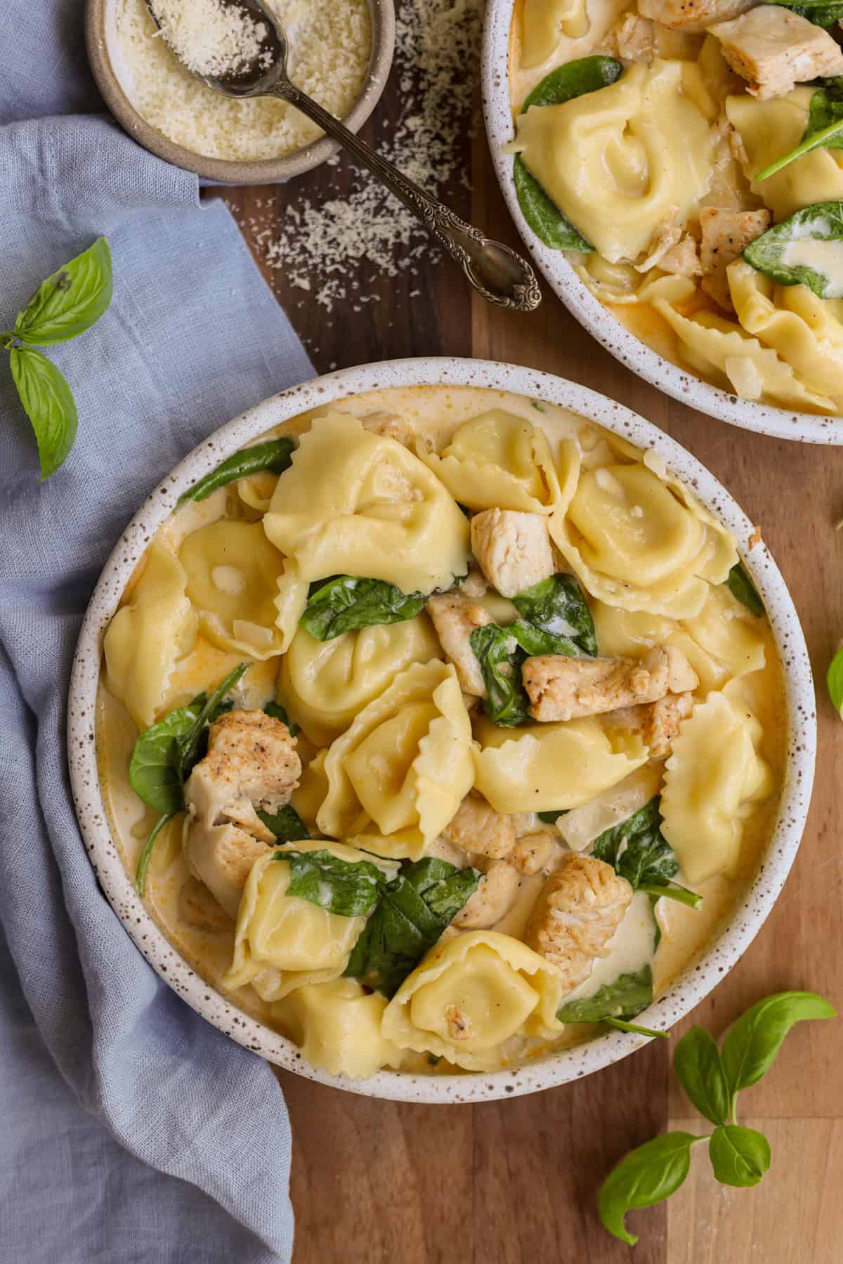 Creamy chicken, tortellini and spinach in a small bowl, garnished with fresh basil and grated parmesan cheese.