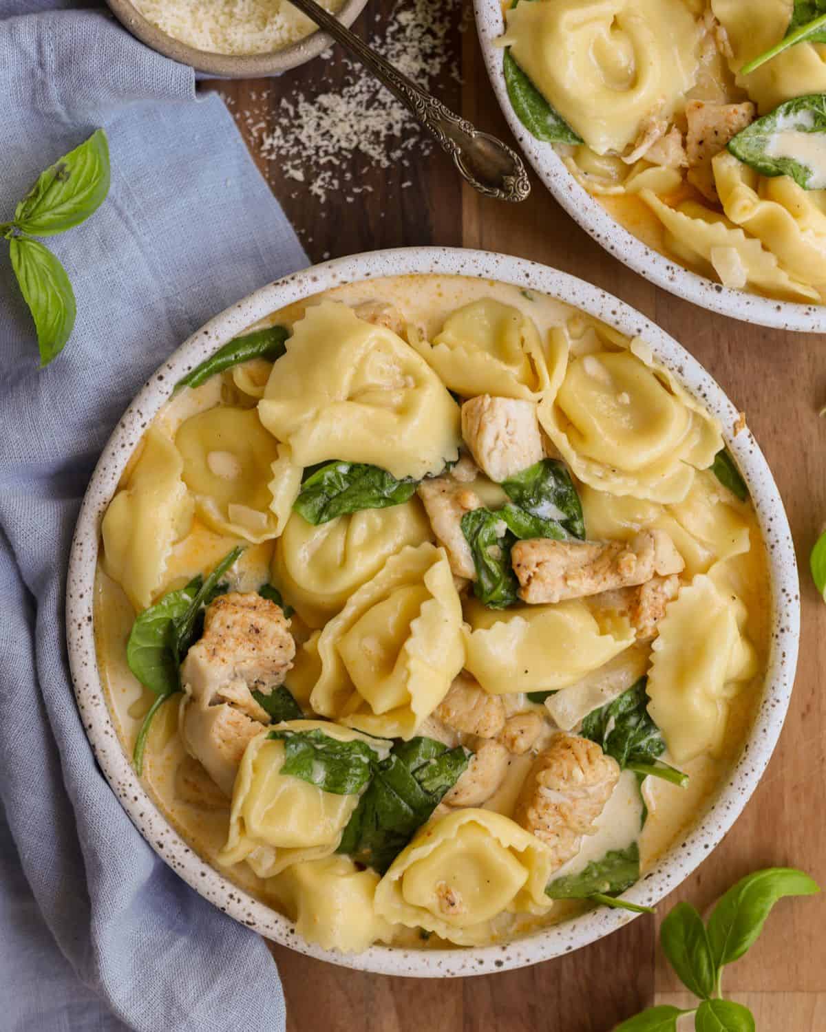 Chicken tortellini with cream sauce and spinach in a bowl with a blue napkin.