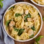 Creamy chicken tortellini in a bowl with a blue napkin and basil garnish.