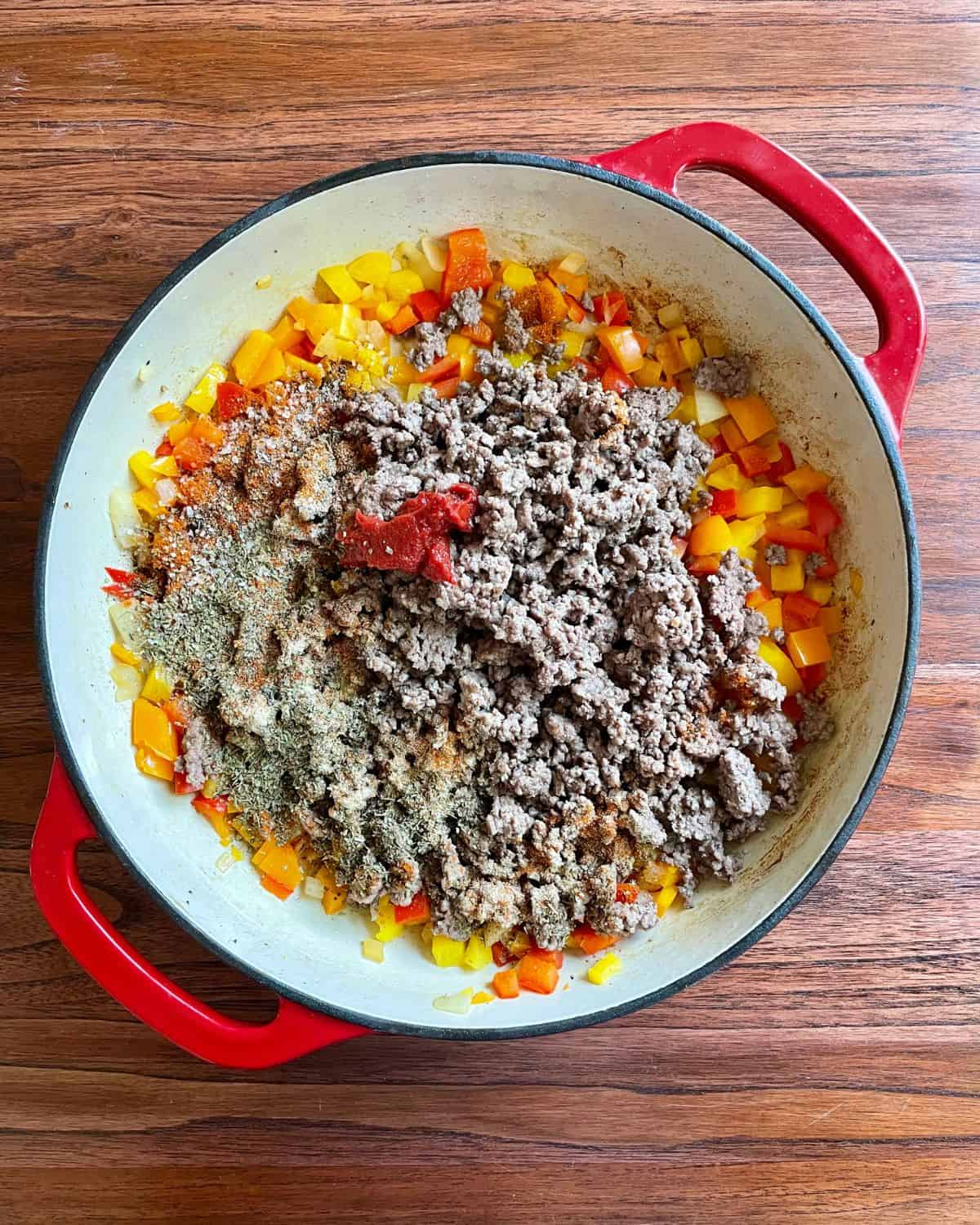 Ground beef, peppers, onions, tomato paste, and seasoning mixing in a skillet.