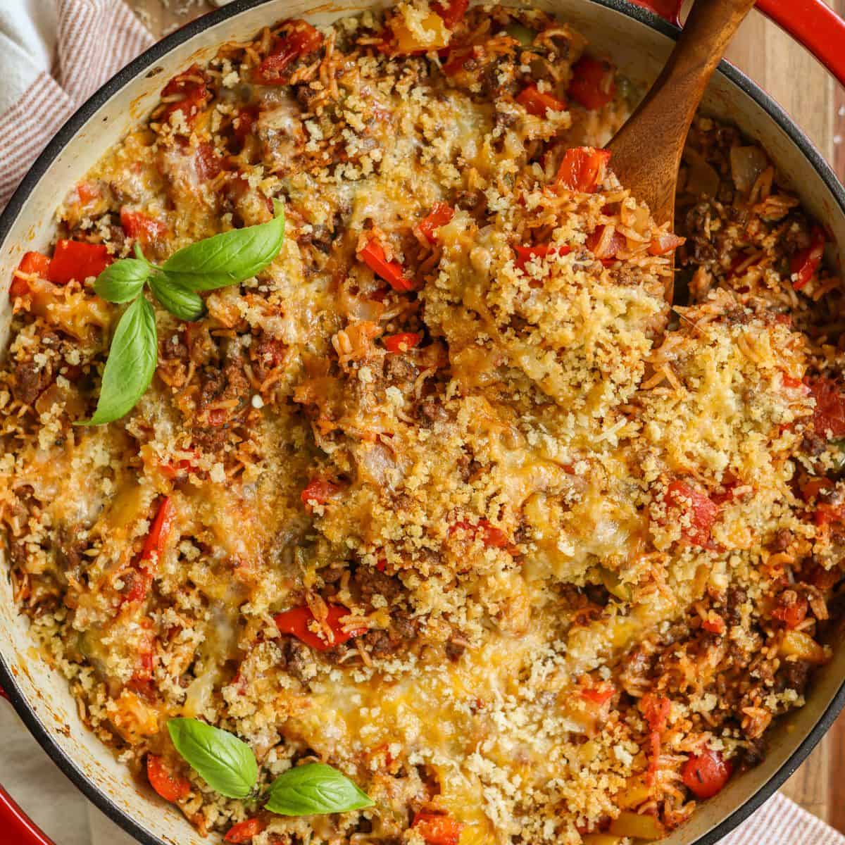 Stuffed peppers skillet in a red dish with a wooden spoon.