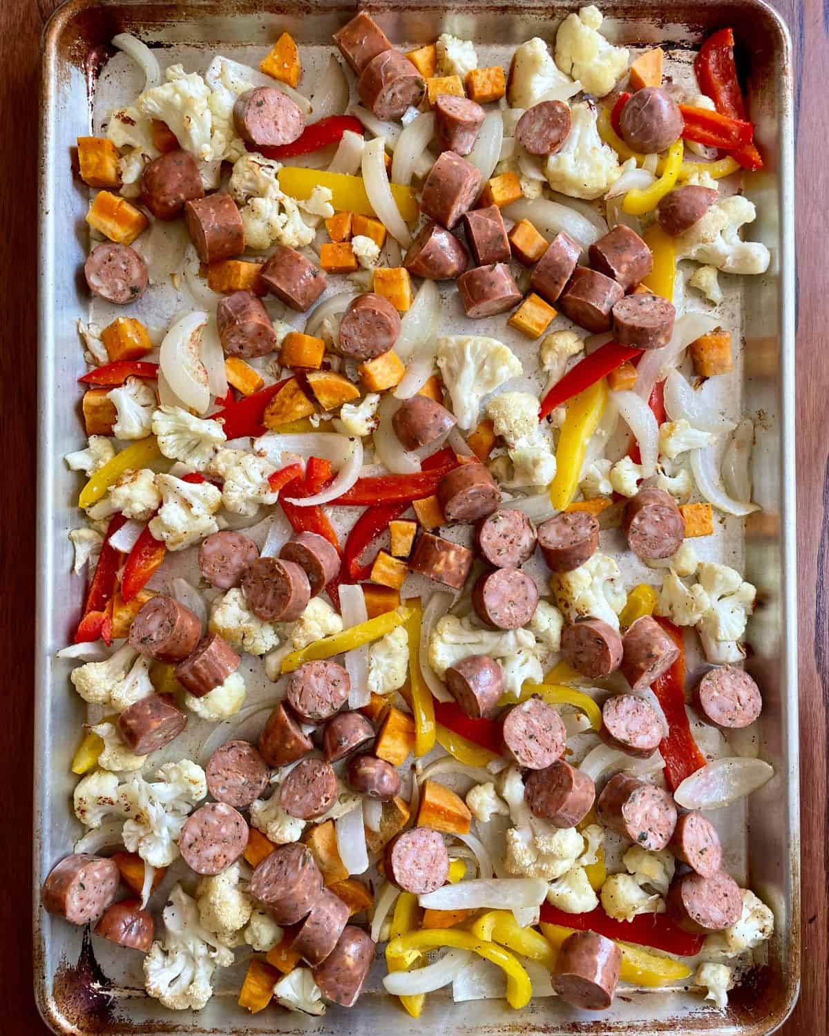 The chopped vegetables are partially roasted and are now tossed with sliced chicken sausage pieces.