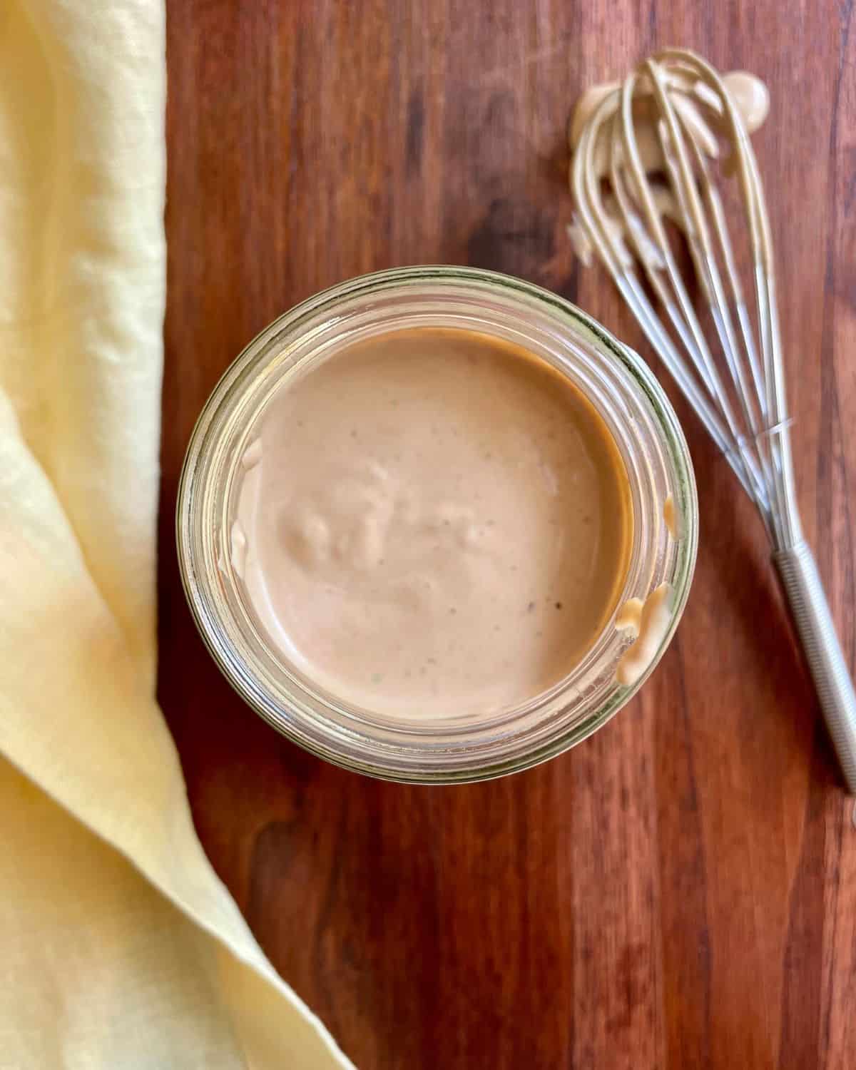 Creamy balsamic dressing in a jar with a whisk and yellow napkin.