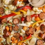 Sheet pan veggies and chicken sausage on the pan, with a small dish of creamy balsamic dressing on the side.