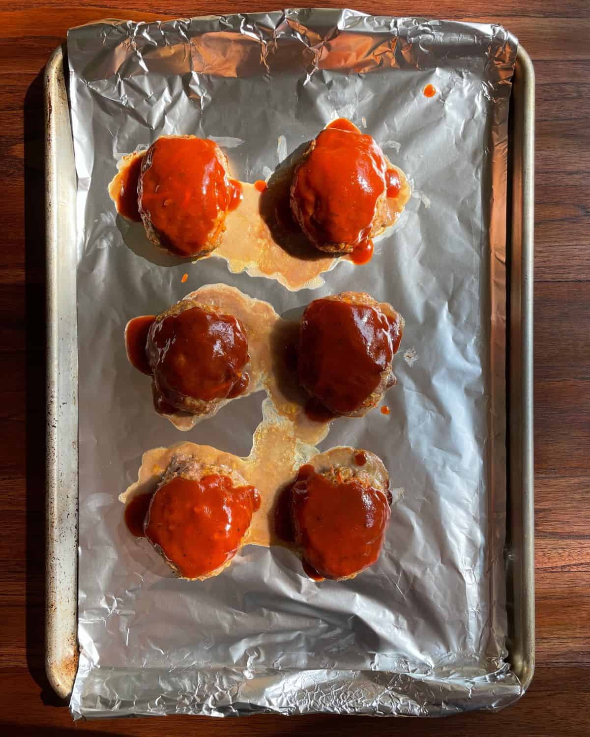 Baked turkey meatloaves brushed with BBQ sauce, on a baking sheet.