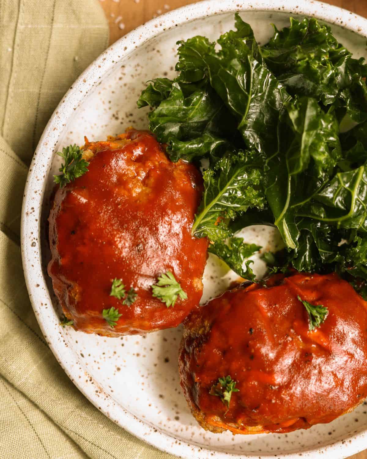 Close-up shot of small turkey meatloaves on a plate. Served with kale.