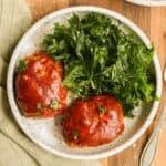 Mini turkey meatloaves brushed with BBQ sauce, on a plate, served with fresh kale.