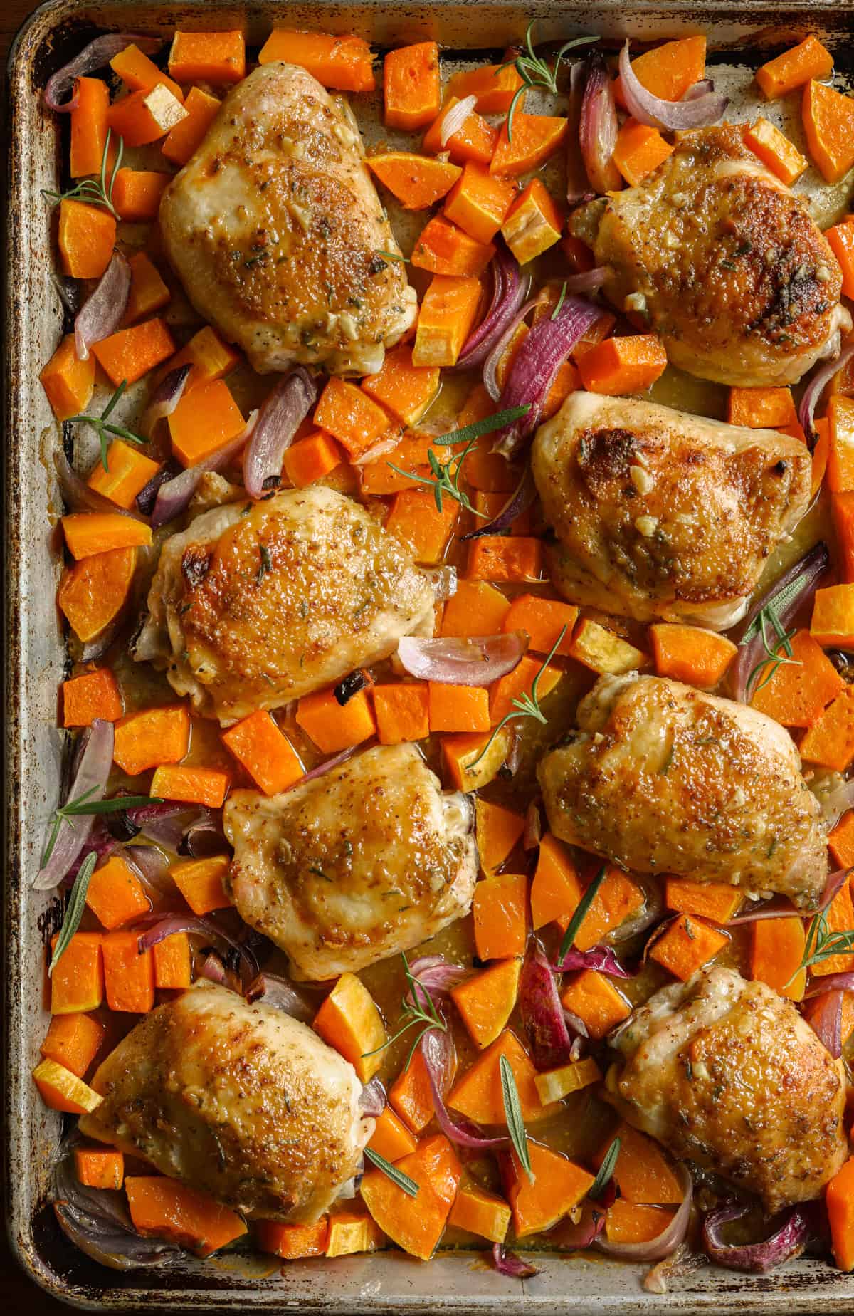 Roasted bone-in chicken thighs on a sheet pan with butternut squash and sliced red onions.