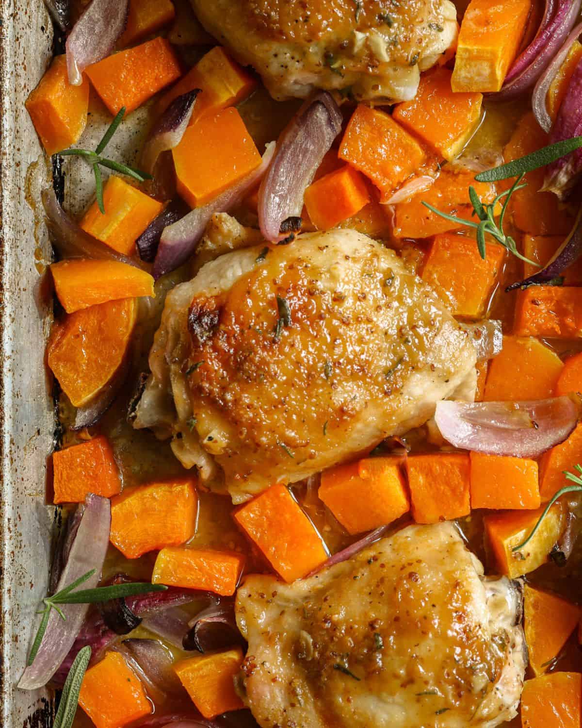 An up-close image of maple mustard glazed chicken thighs and butternut squash on a sheet plan.