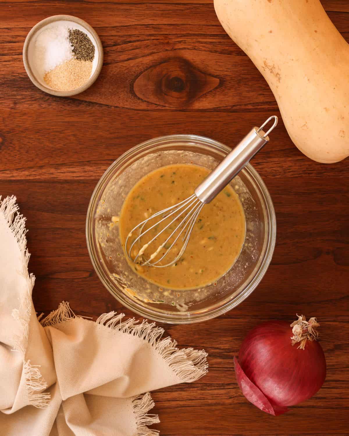 Maple mustard glaze mixed up in a glass bowl with various ingredients scattered around the image.