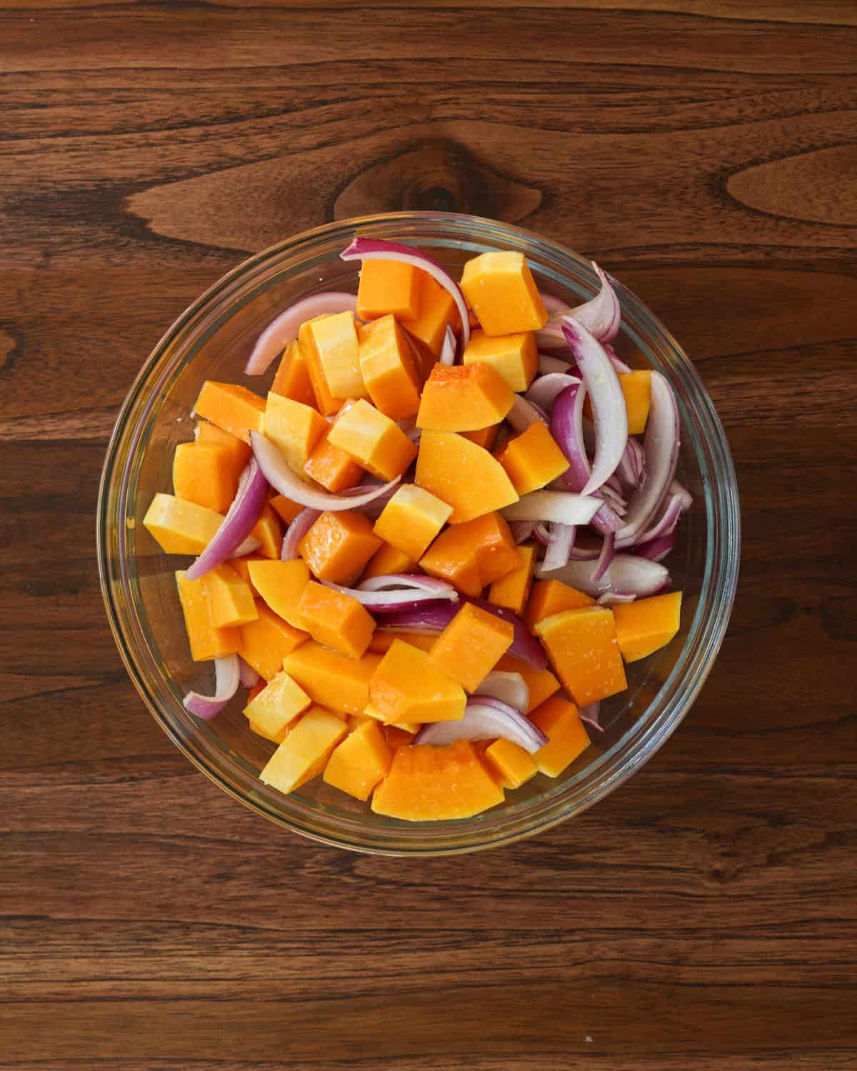 Chopped and peeled butternut squash and sliced red onion in a bowl.