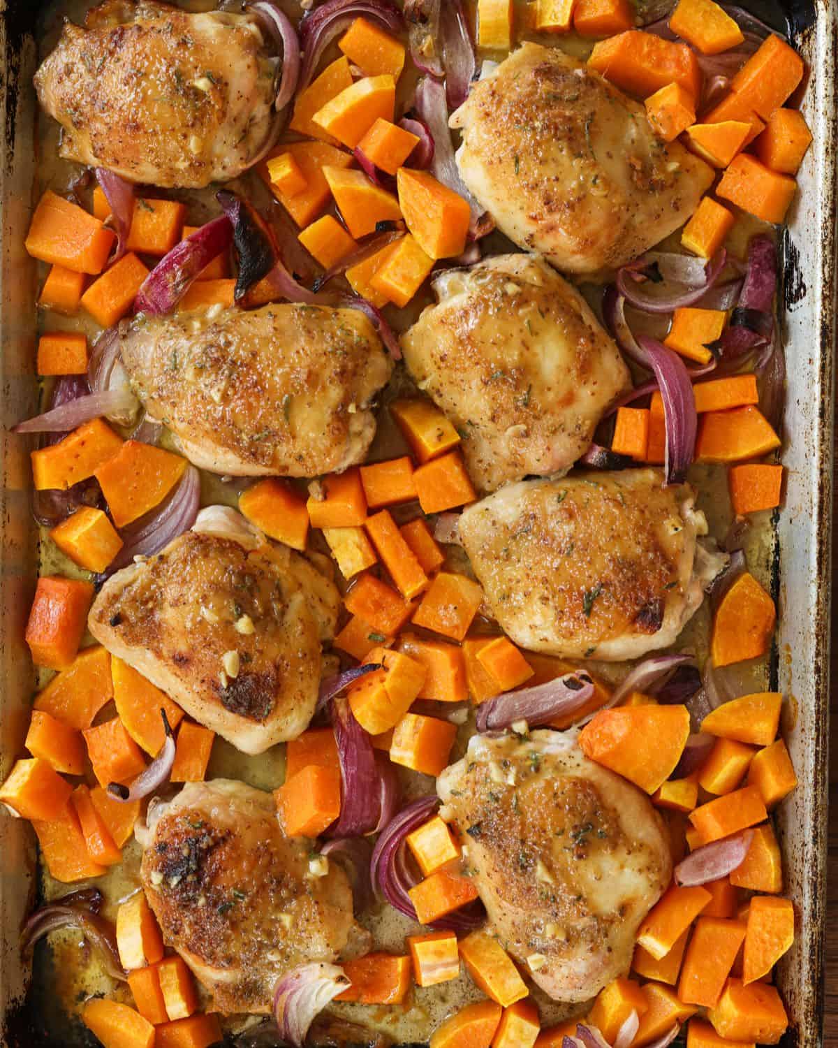 Cooked chicken thighs and squash on a baking sheet, right after it has come out of the oven.