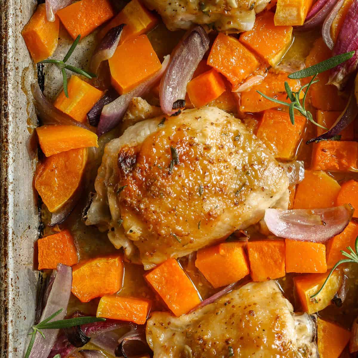 A zoomed in image of maple mustard chicken thighs and butternut squash on a baking sheet.