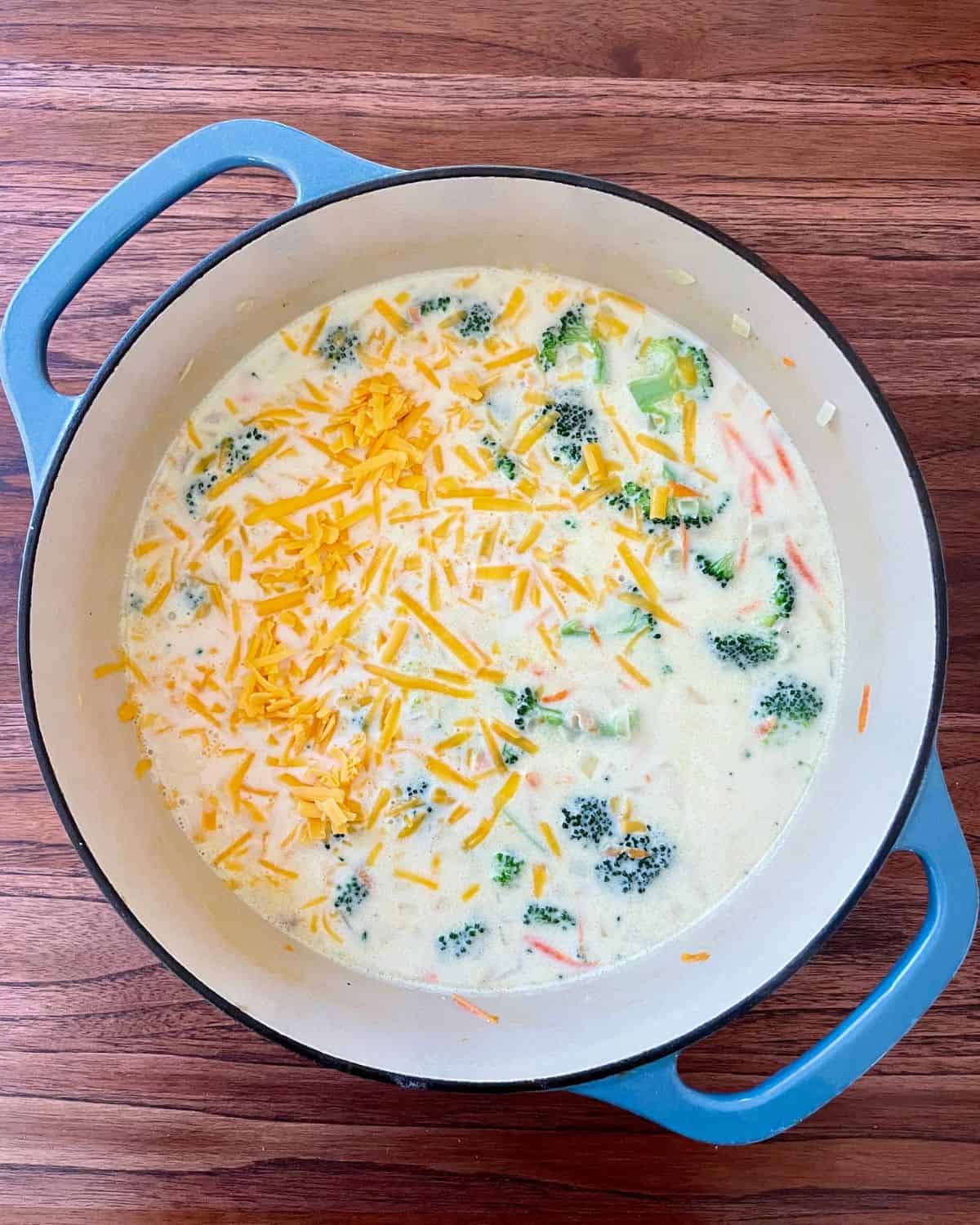 The soup ingredients are mixed together and simmering in a Dutch oven. Shredded cheese has just been added to the pot.