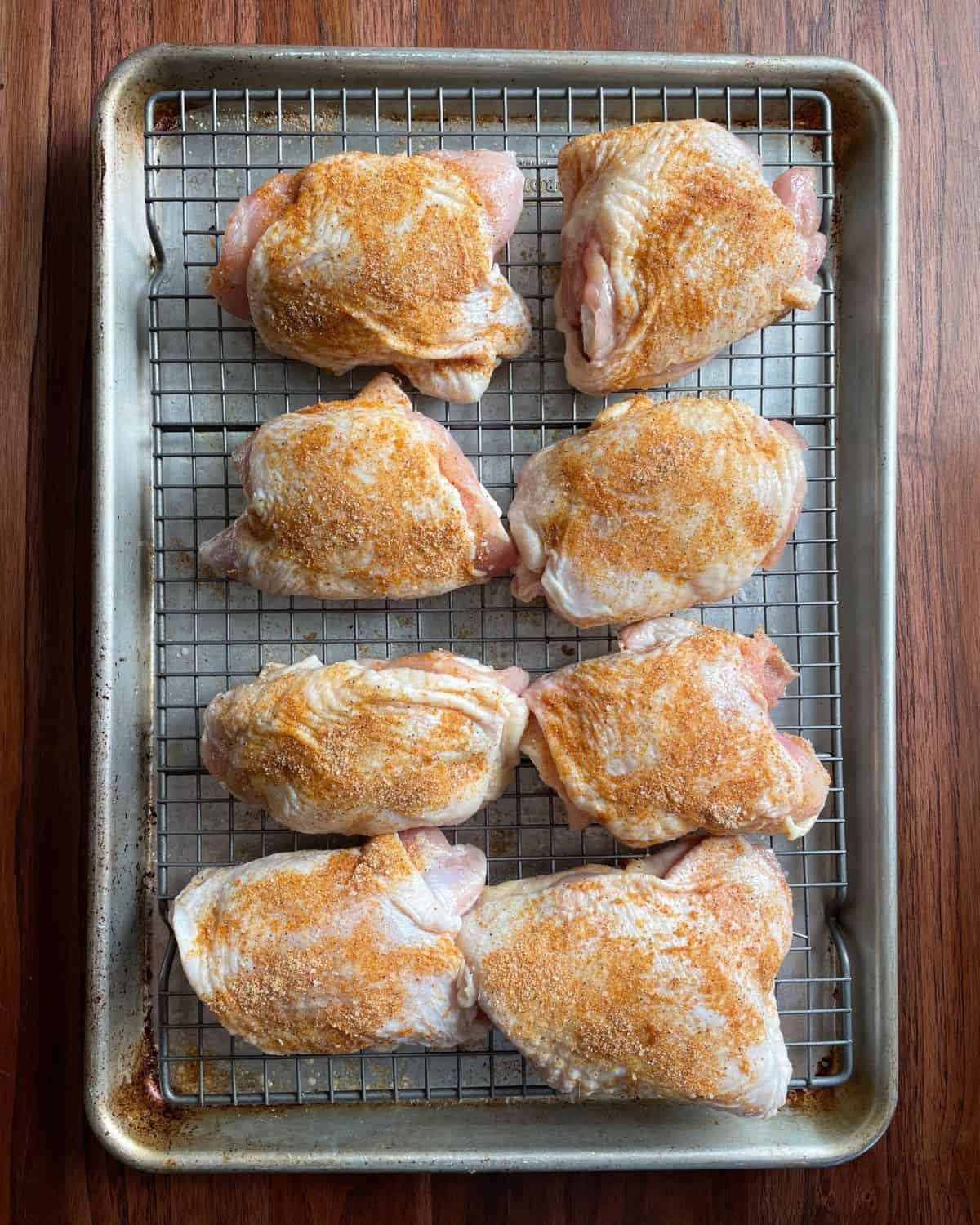 Bone-in chicken thighs on a wire-lined baking sheet, seasoned and ready to bake.