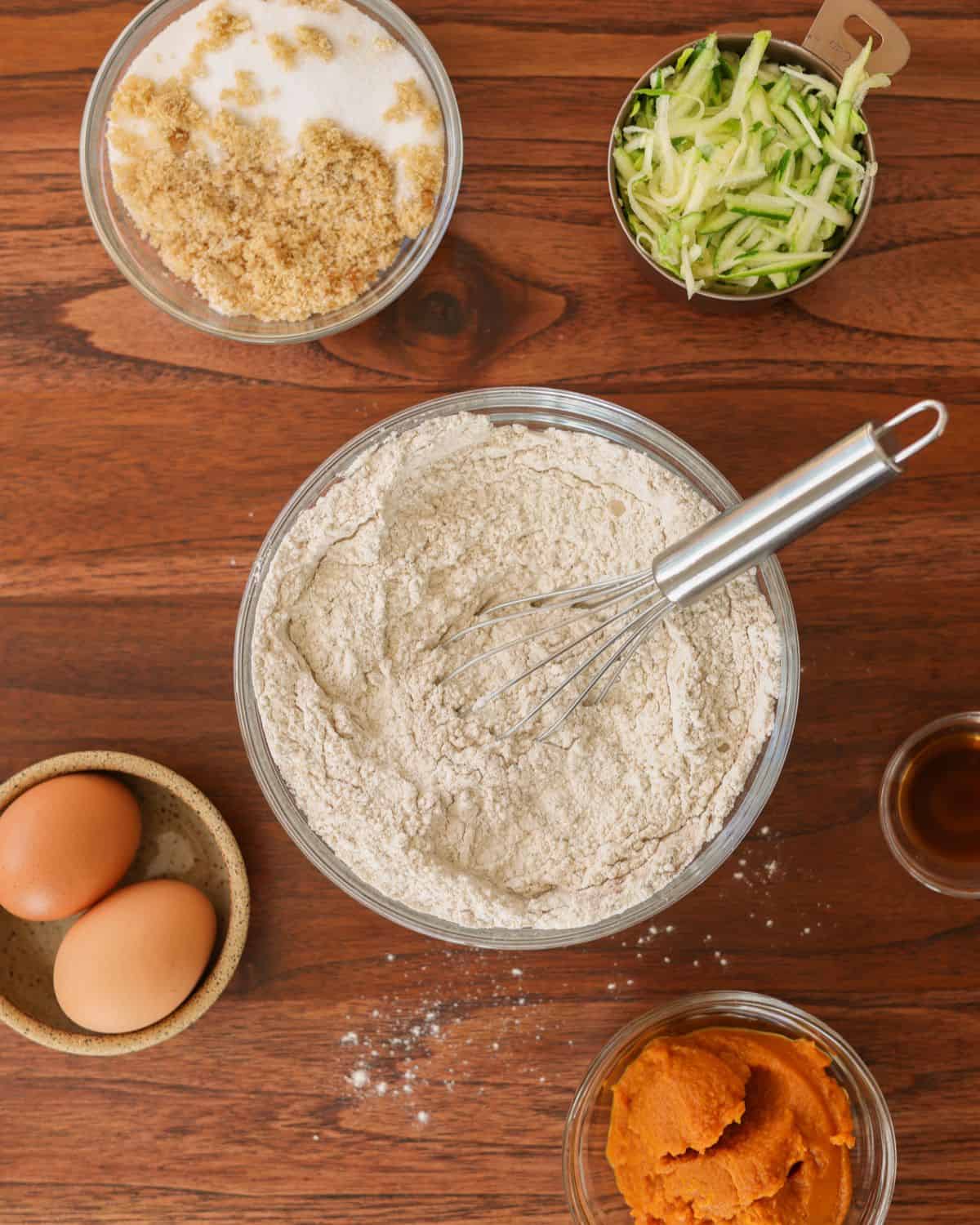 Dry ingredients combined in a glass bowl. The rest of the muffin ingredients are scattered around the bowl.