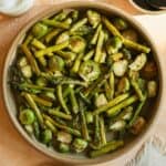 Roasted asparagus and Brussels sprouts in a dish with balsamic glaze on the side.