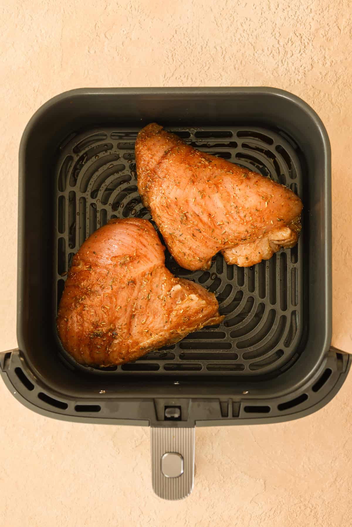 Two raw turkey tenderloins in an air fryer basket, seasoned and ready to cook.