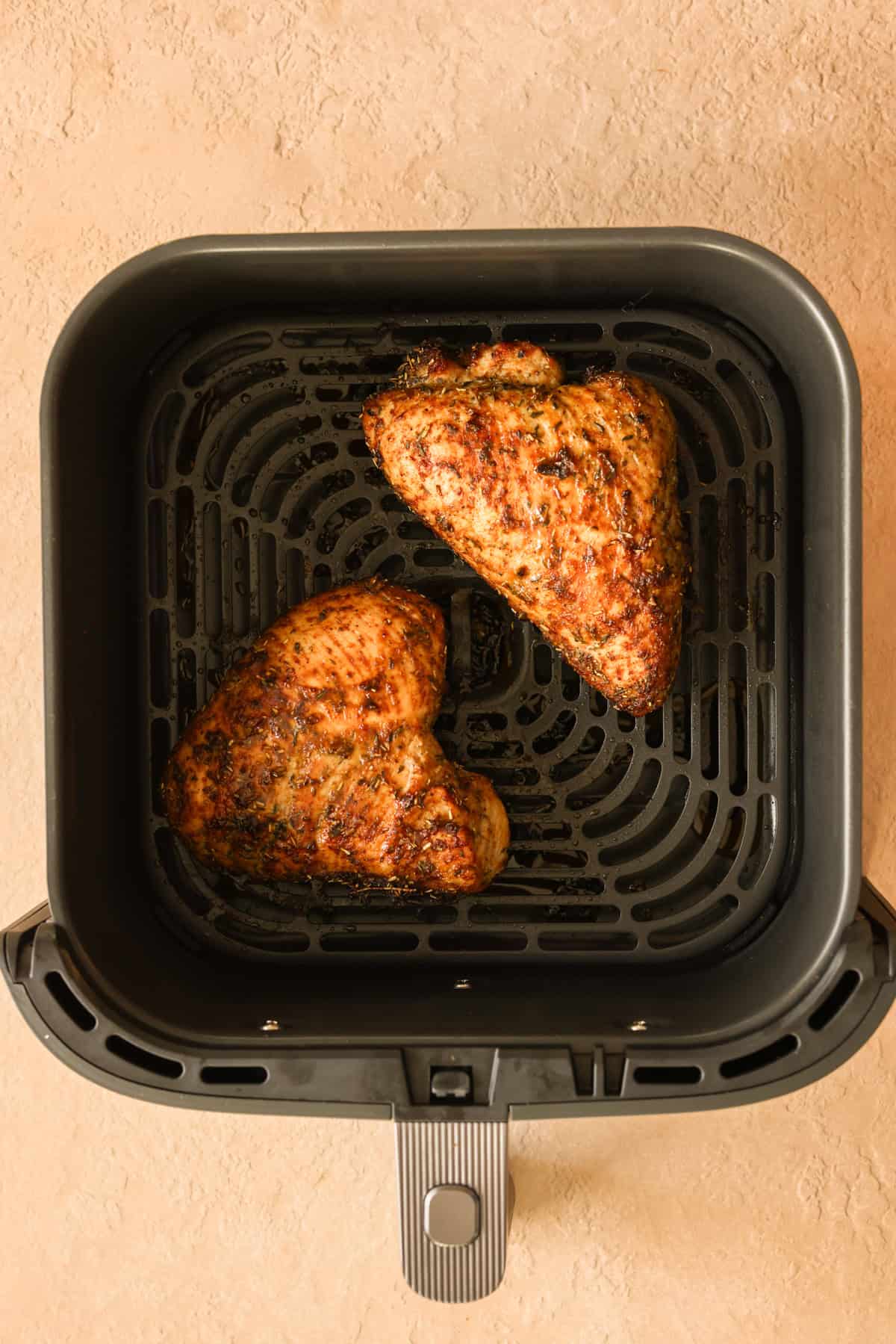 Two turkey breast tenderloins fully-cooked in an air fryer basket.