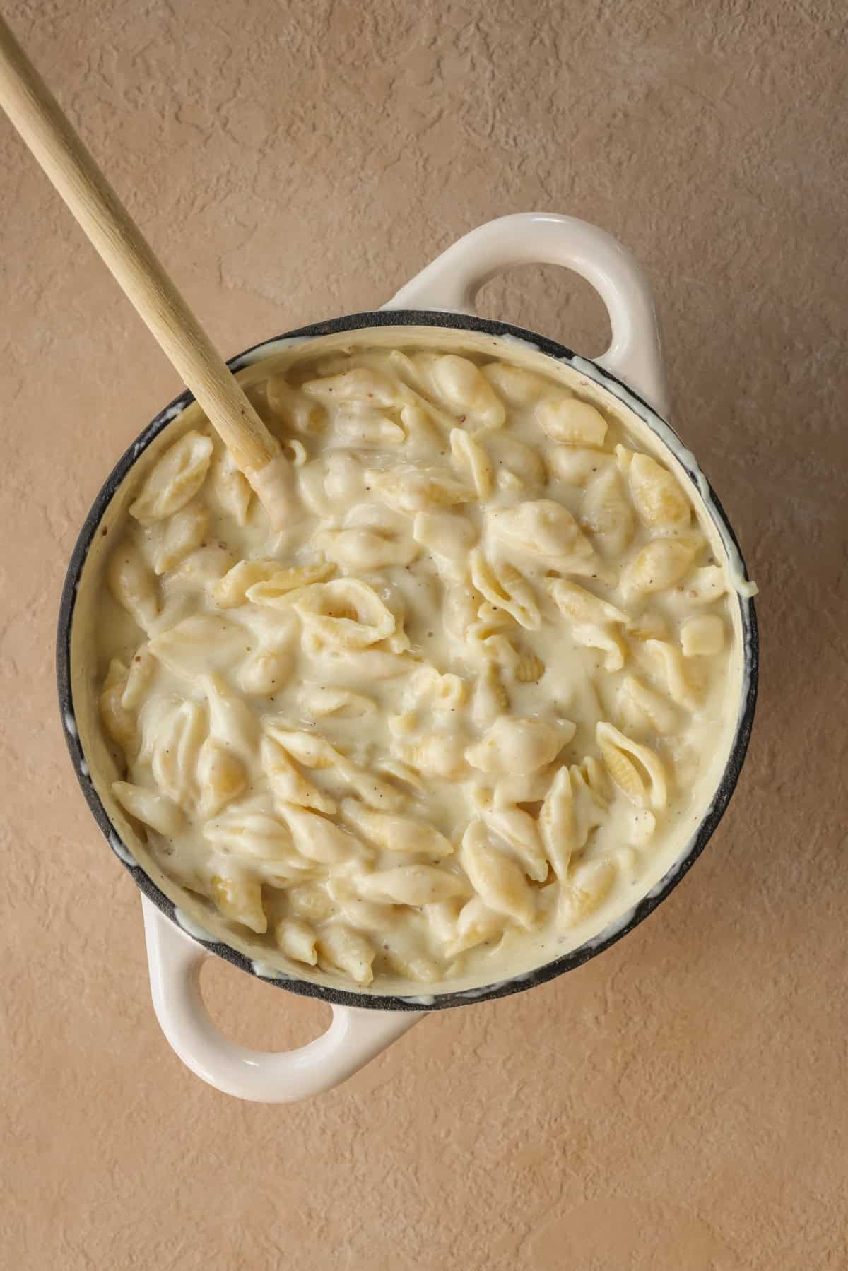 Fully cooked creamy macaroni and cheese in a cast iron pot with a wooden spoon.