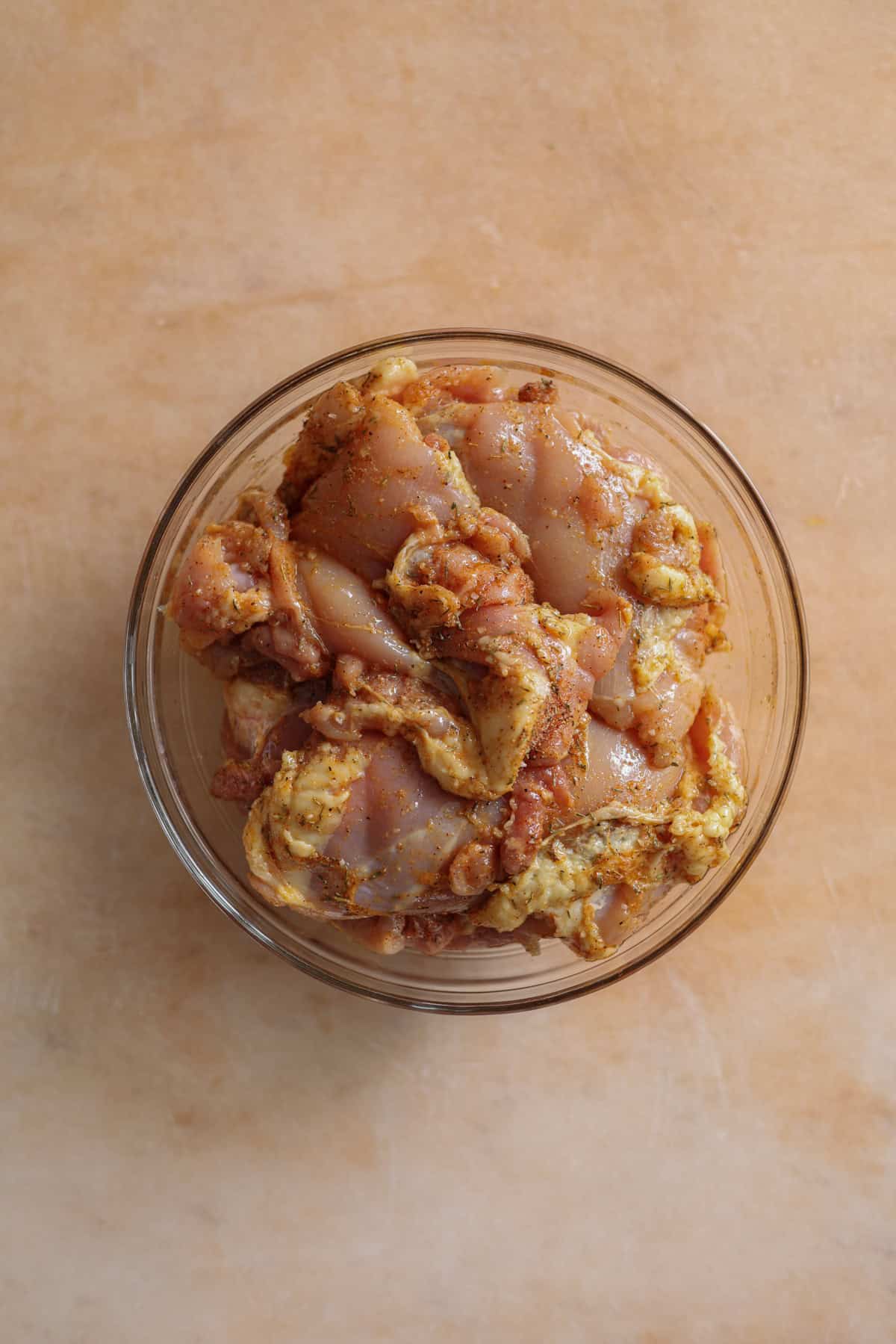 Boneless chicken thighs seasoned with various spices, in a glass bowl.