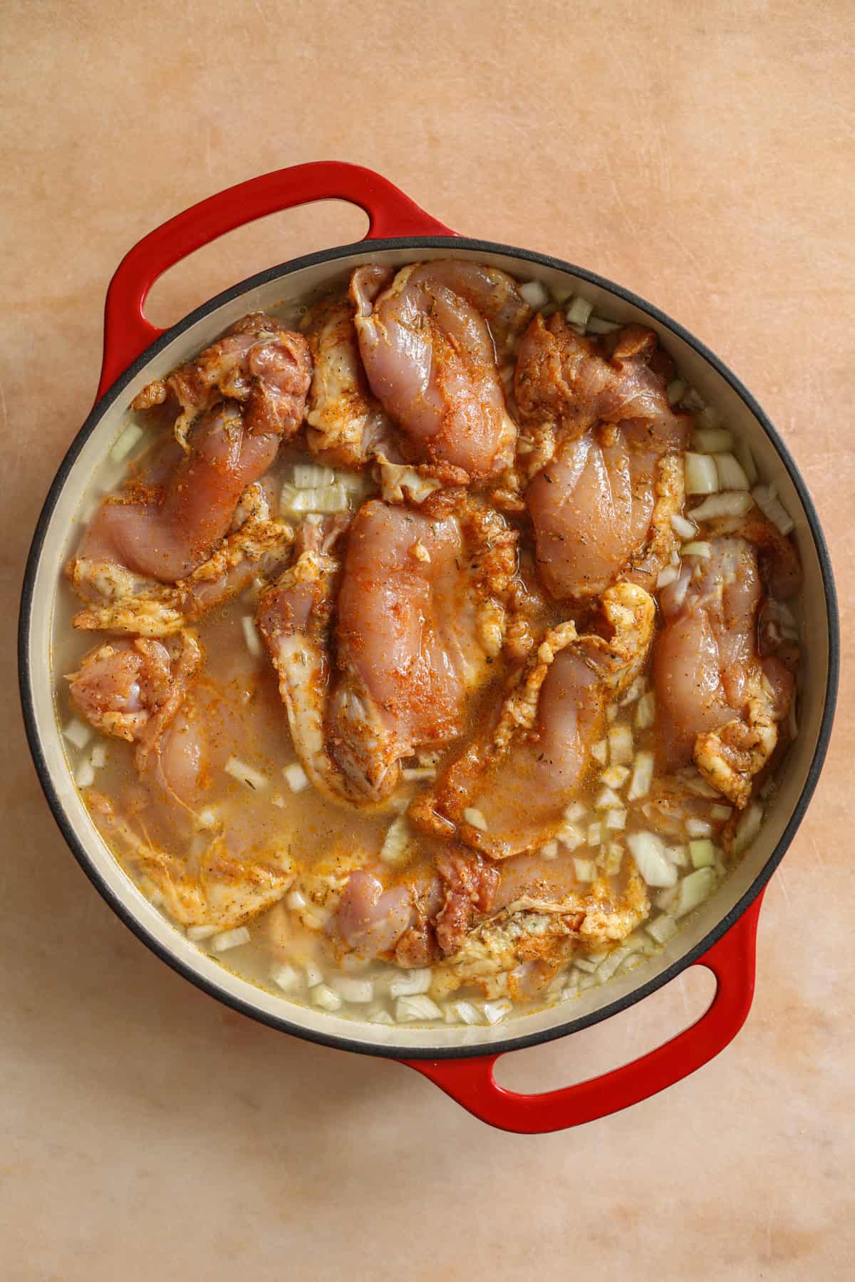 Uncooked boneless chicken thighs laid on top of the rice, onions, and water. It's ready to go in the oven to be baked.