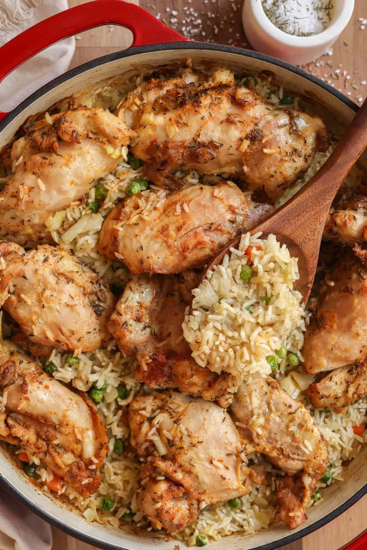 Baked boneless chicken thighs and basmati rice in a skillet. Some rice is being scooped up with a wooden spoon.