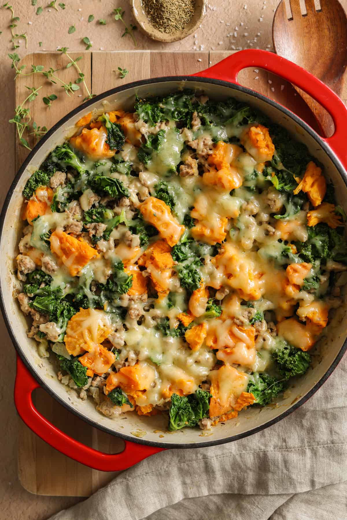 A ground turkey and sweet potato skillet dinner topped with shredded cheese in a large, cast iron dish.
