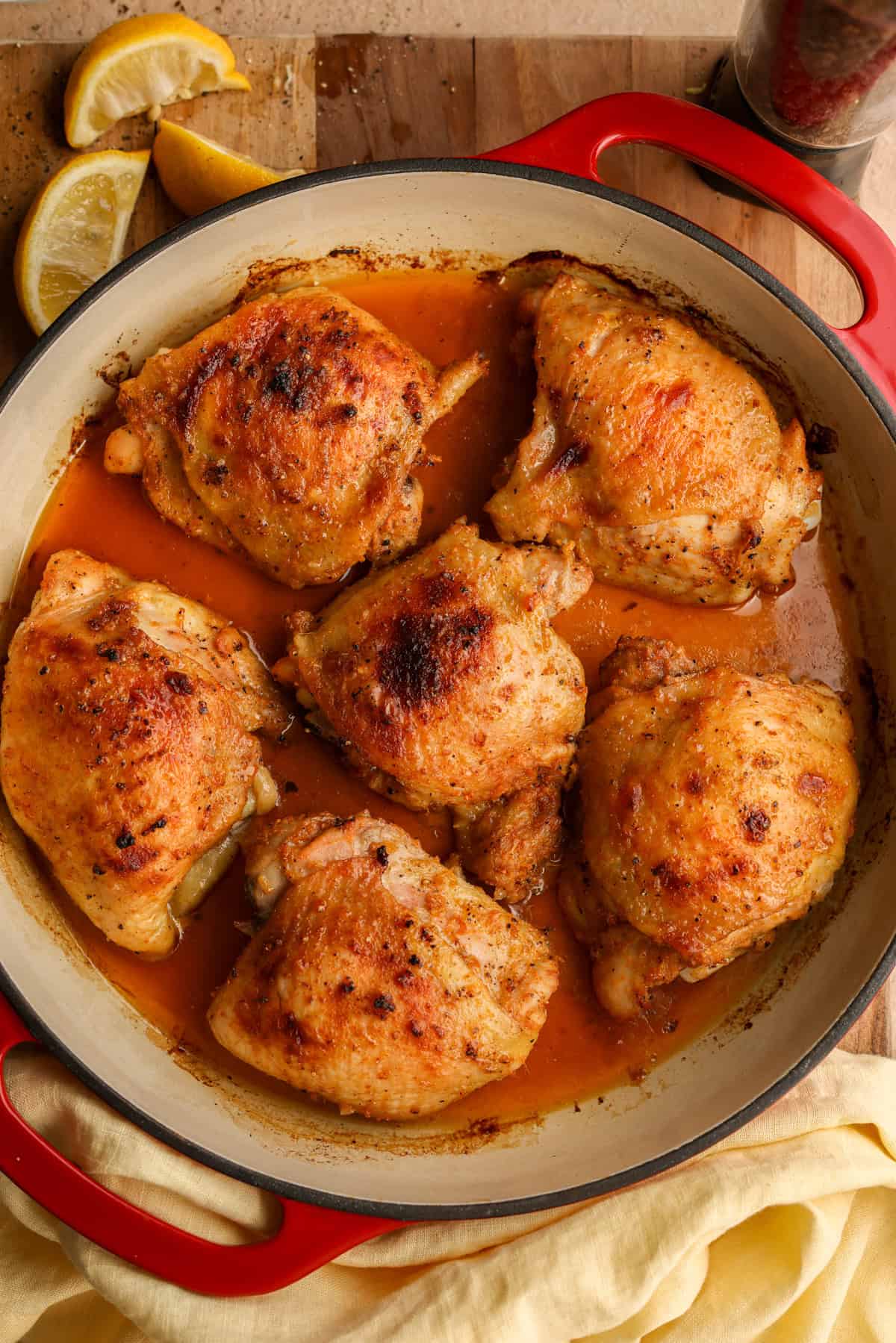 Lemon, pepper, honey, and olive oil smothered chicken thighs in a red, cast iron braising dish.