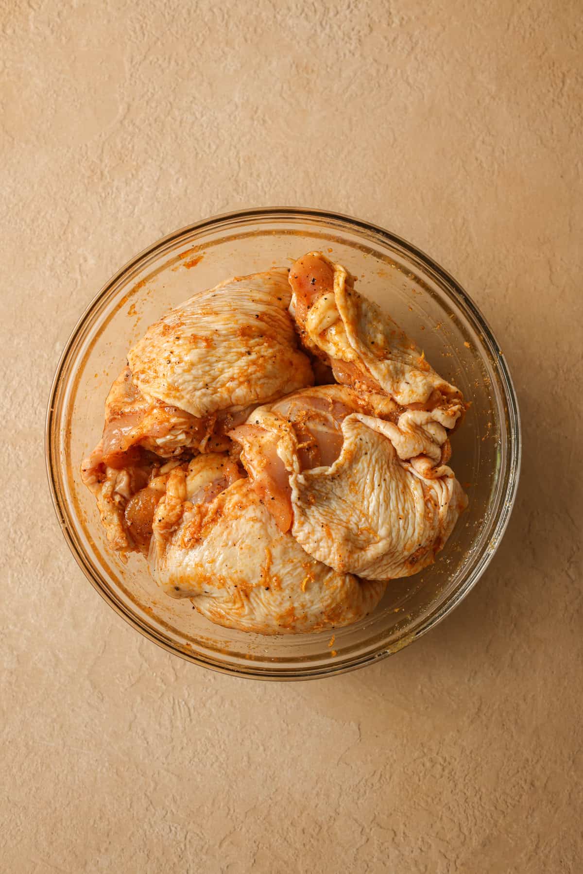 Chicken thighs in a dish covered with lemon pepper seasoning.