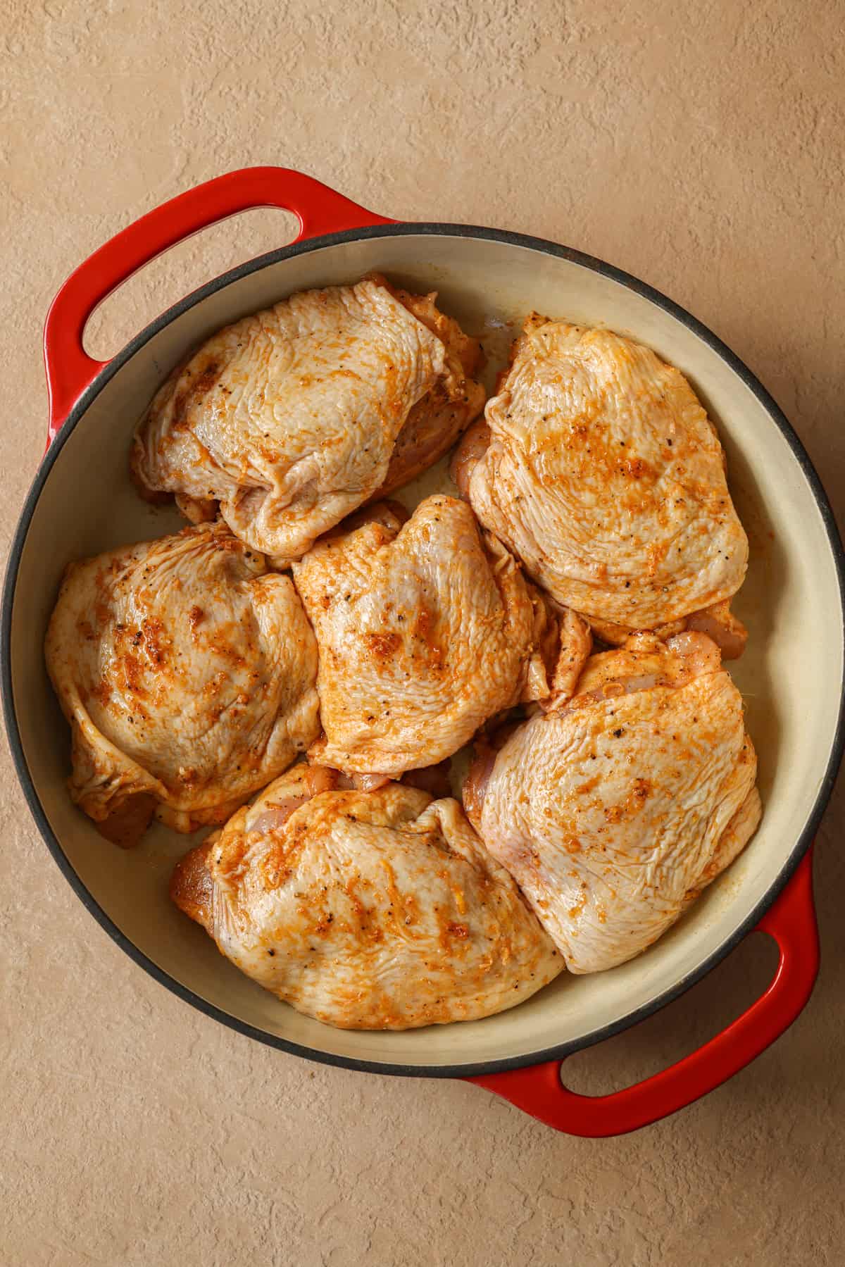 Bone-in chicken thighs in a baking dish, smothered with lemon pepper seasoning.