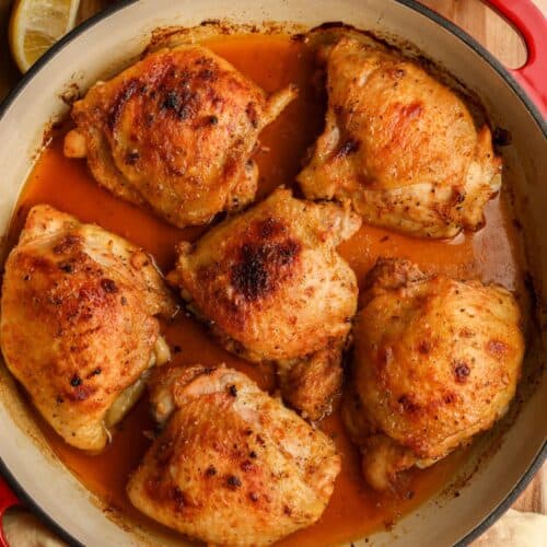 Pepper and lemon chicken thighs in a red braising dish.