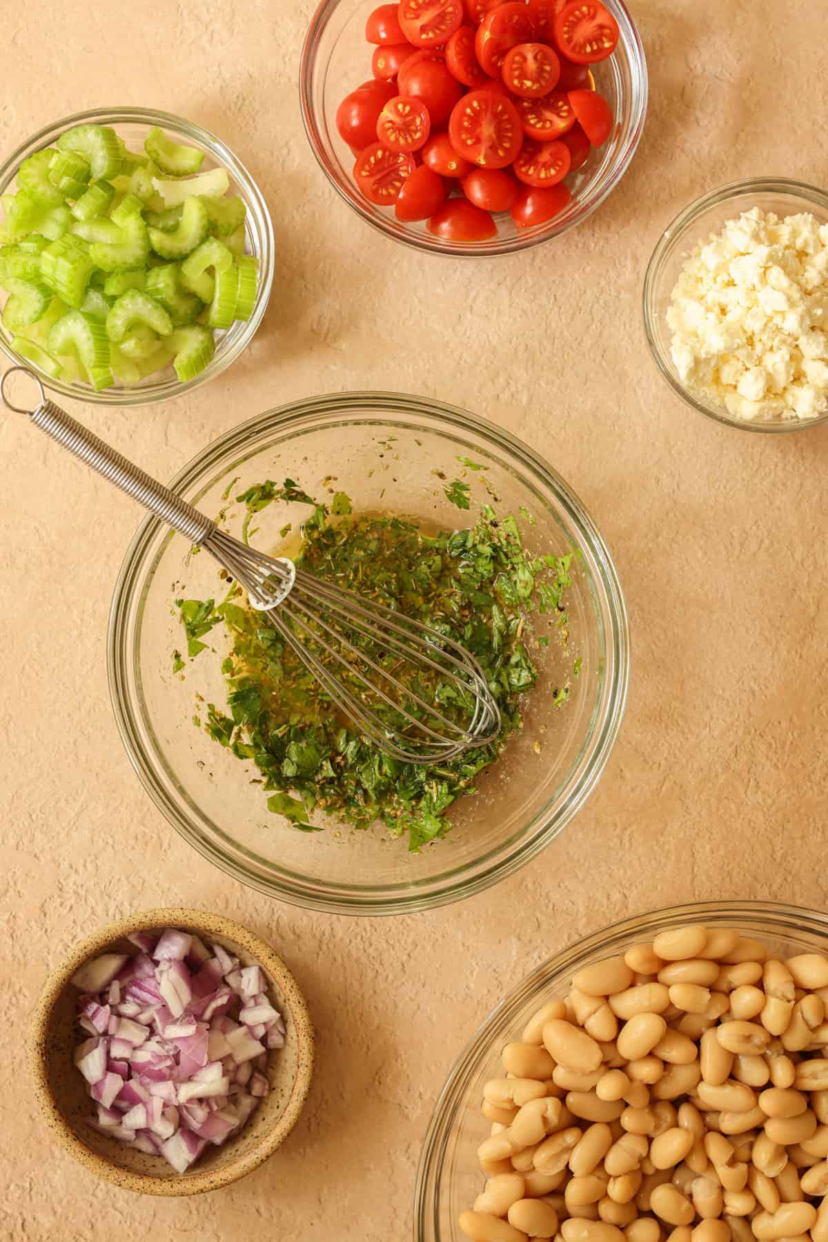 The white bean salad dressing is whisked together in a small glass dish. The rest of the salad ingredients are on the side in small dishes, ready to be combined.