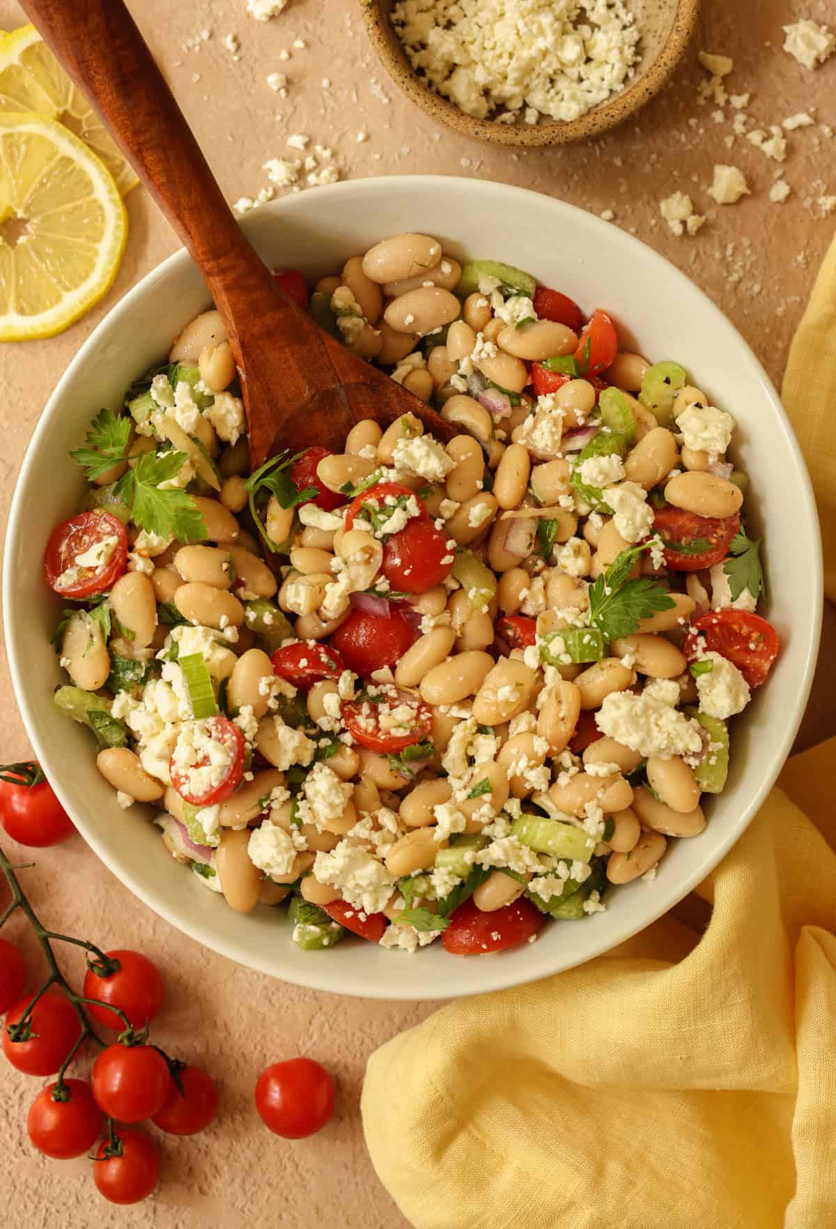Mediterranean white bean salad, ready to serve. The salad is garnished with an extra sprinkle of parsley, lemons, and feta cheese.