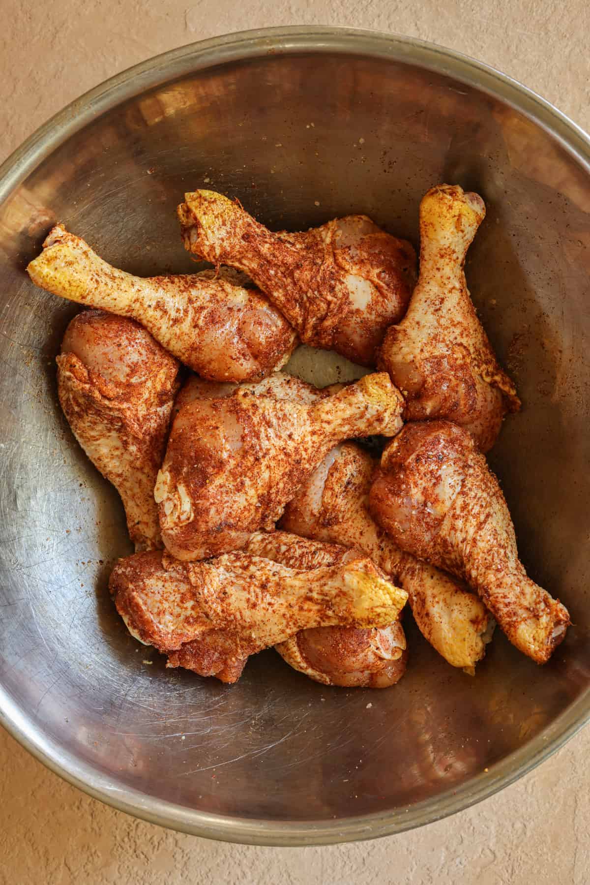 Chicken drumsticks in a large bowl, tossed in BBQ seasoning.