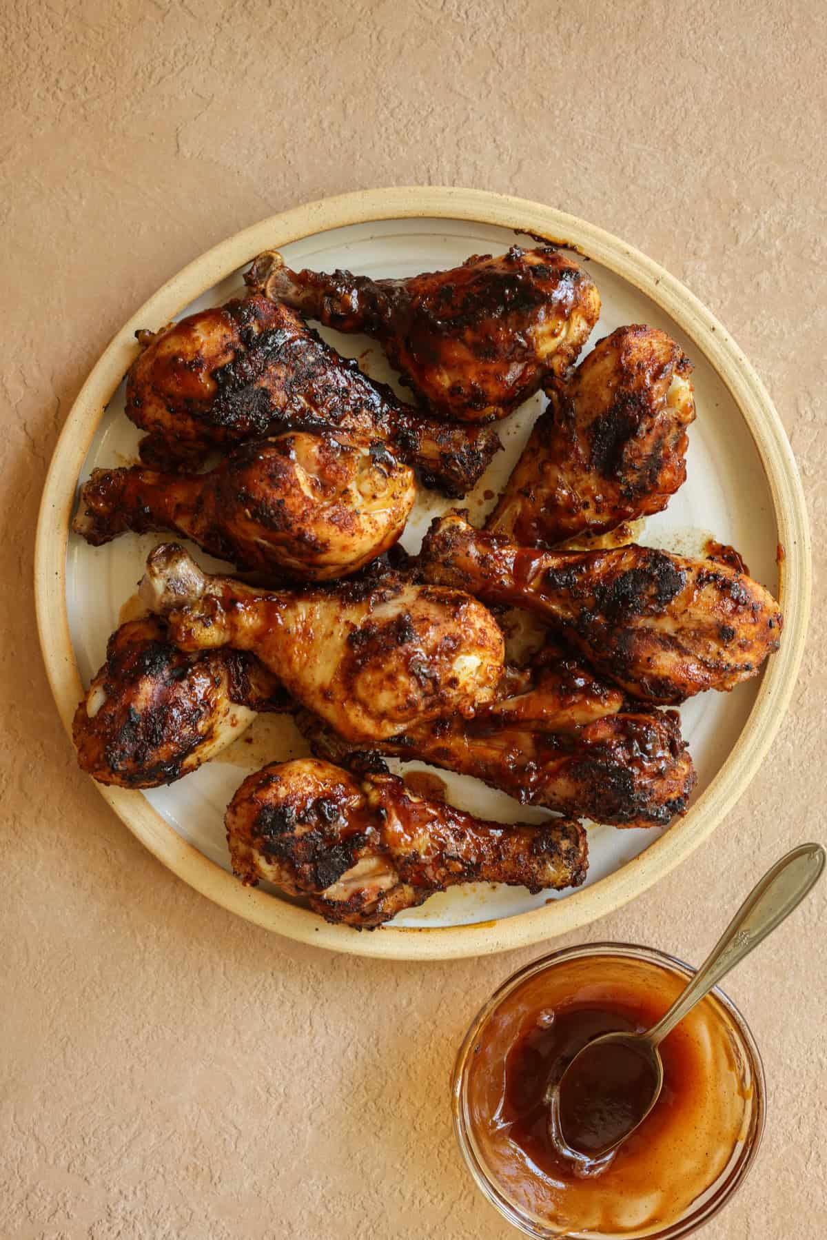Grilled chicken drumsticks brushed with BBQ sauce, on a plate, with a small bowl of extra BBQ sauce on the side.