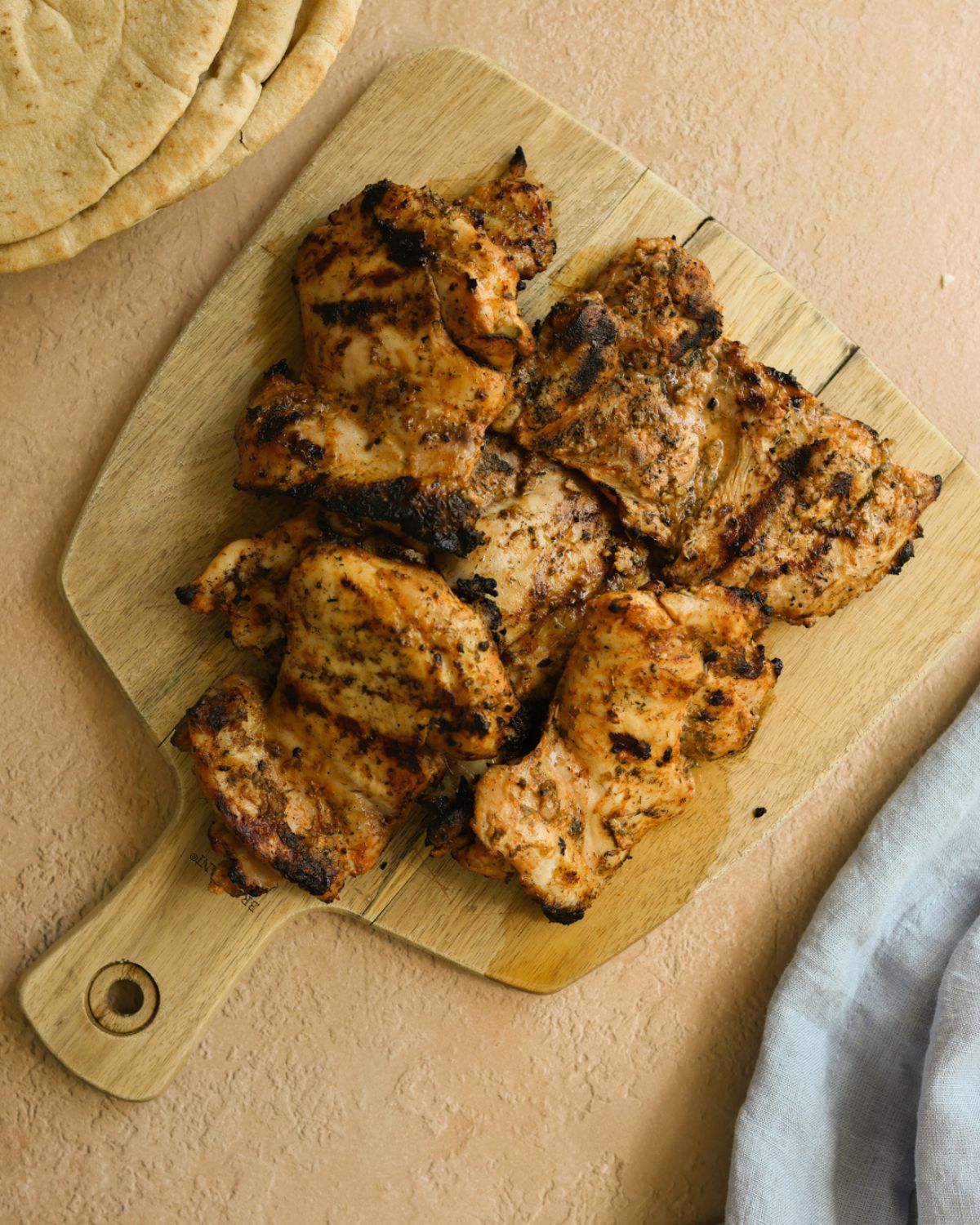 A cutting board stacked with grilled boneless chicken thighs.