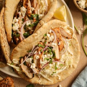 A plate of grilled chicken pitas stuffed with Tzatziki slaw, red onions, and feta cheese.
