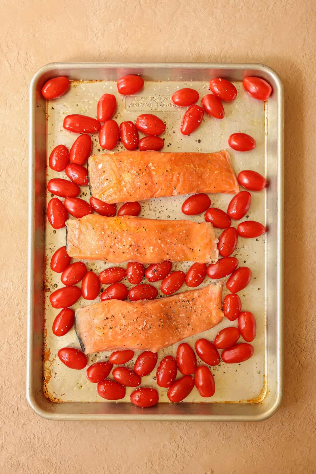 A sheet pan of frozen salmon filets and cherry tomatoes seasoned with salt and pepper.