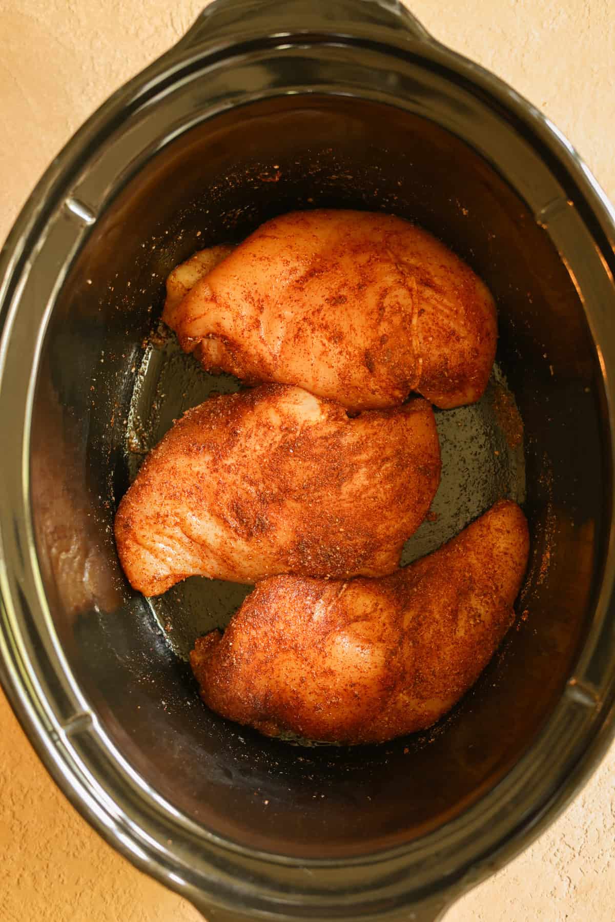 Seasoned chicken breasts in the bottom of a slow cooker.