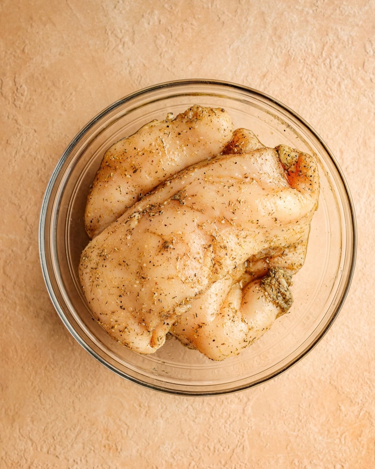 Seasoned chicken breasts in a bowl.