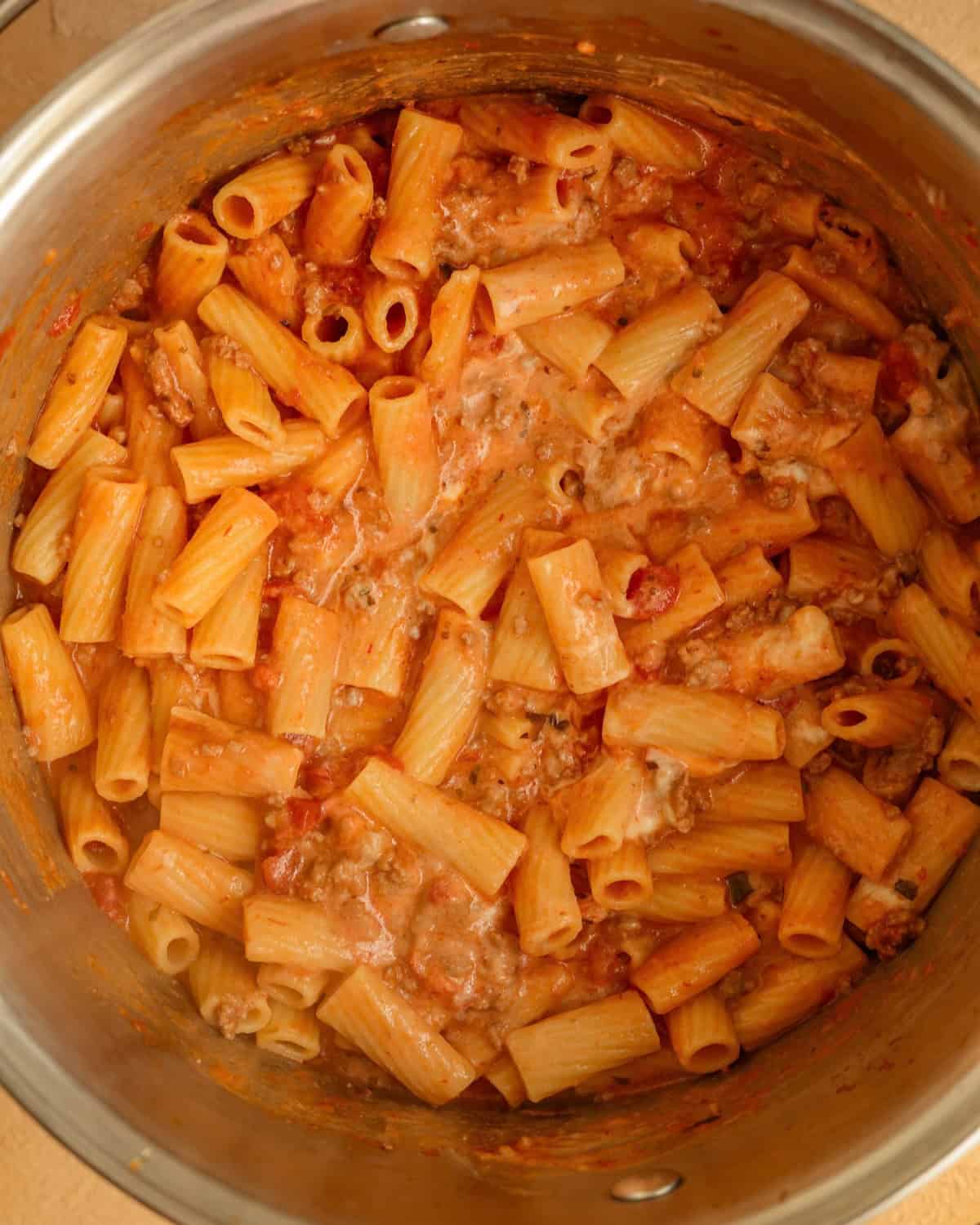 Cooked ziti noodles mixed with ricotta cheese and meat sauce in a large sauce pan.