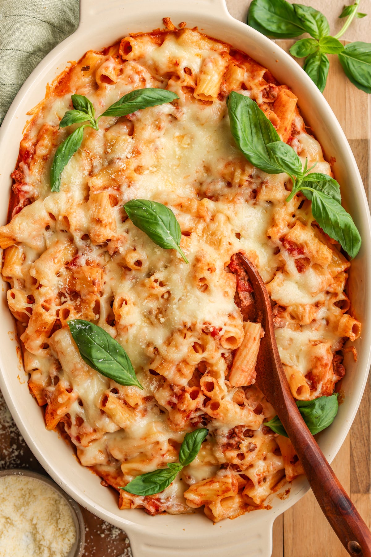 An oval baking dish with an easy baked ziti in it. The ziti has a wooden spoon scooped into the center of it and it's garnished with fresh basil.